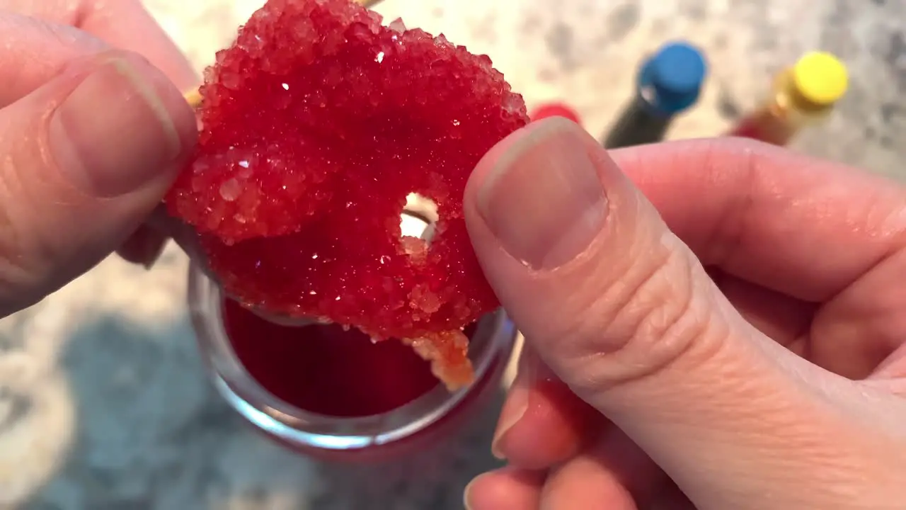 A hand holding a sparkly red Borax crystal