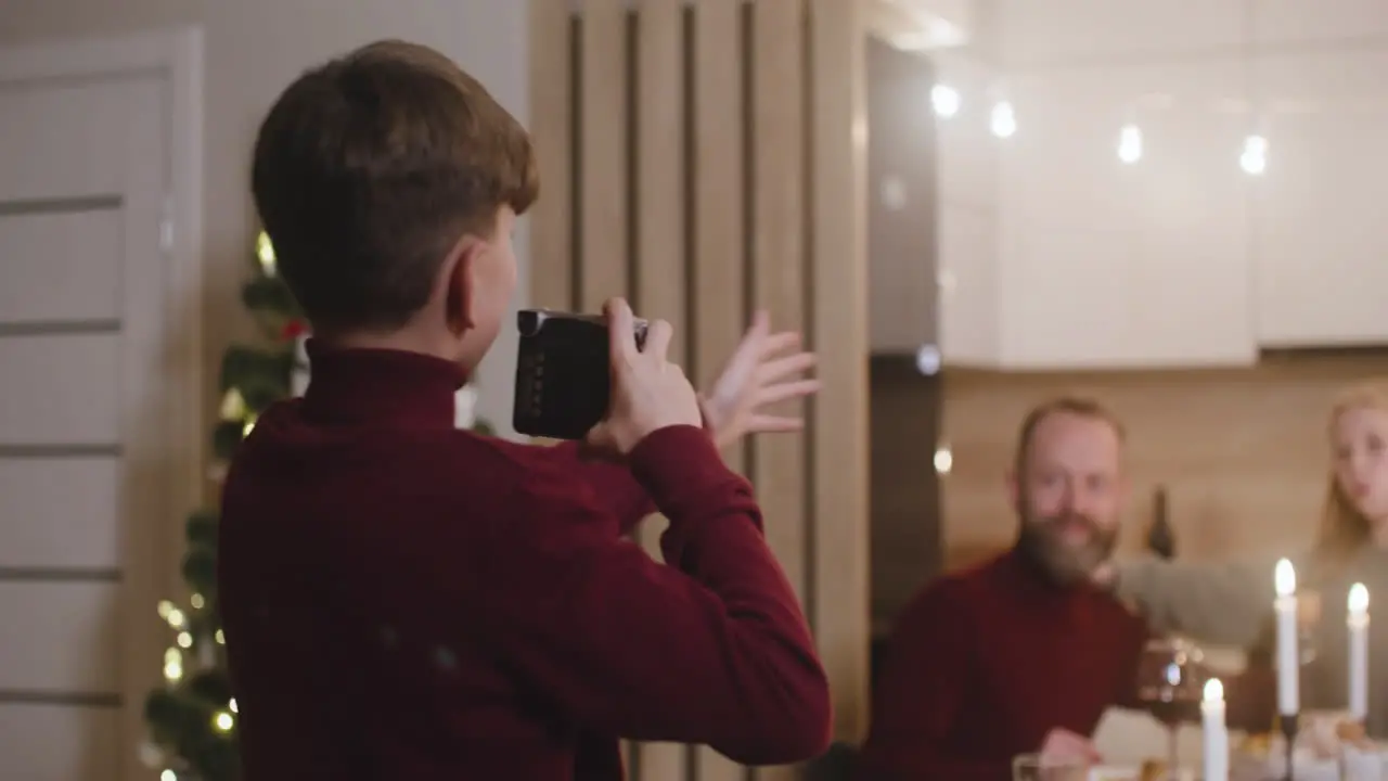 A Blond Boy In A Red Turtleneck Sweater Takes A Picture Of His Parents And Sister Sitting At The Table At Christmas Dinner