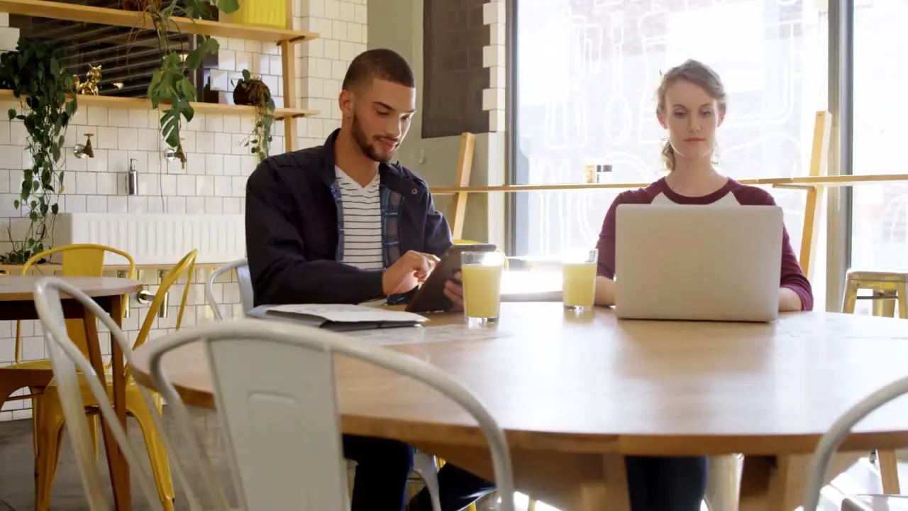 Executives working on digital tablet and laptop in cafeteria 4K 4k