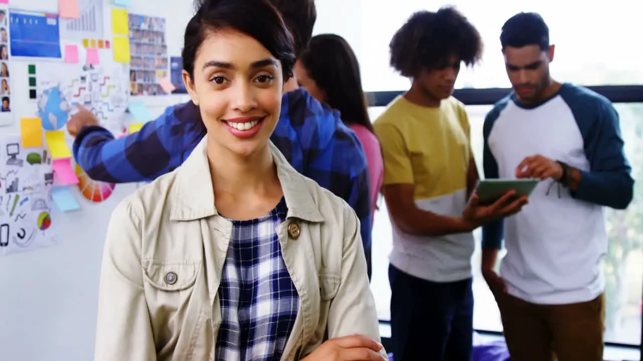 Smiling graphic designer standing with arms crossed while colleague discussing 