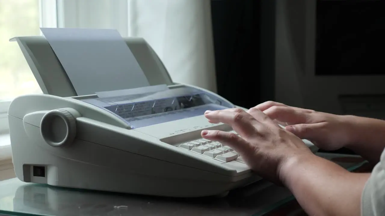 Person Types on a Typewriter Next to a Window in Slow Motion