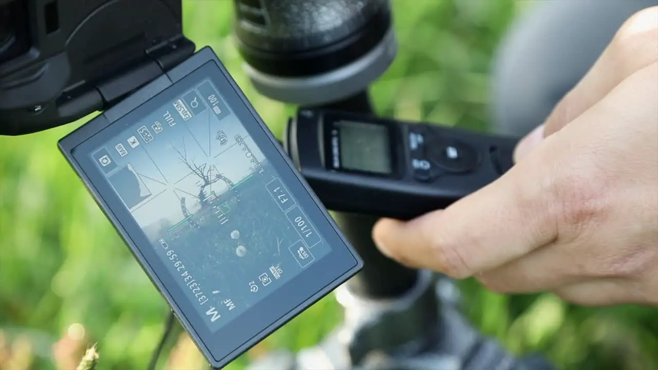 The photographer touches the camera display and holds the intervalometer in the other hand for time-lapse photography