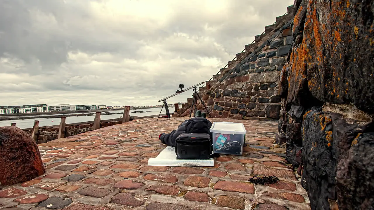 Time lapse of content creator waiting for motion time lapse set up on slider to finish clouds flying through sky in Guernsey