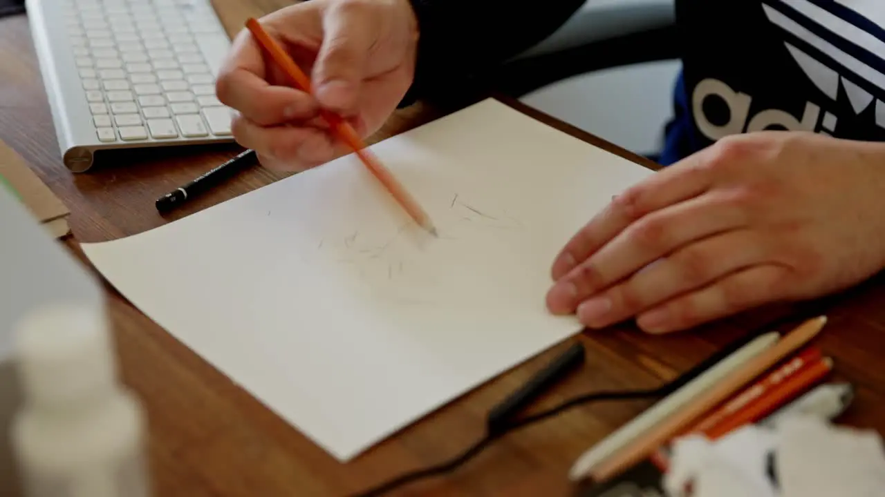 A young man chooses a pencil to continue his sketch of a face