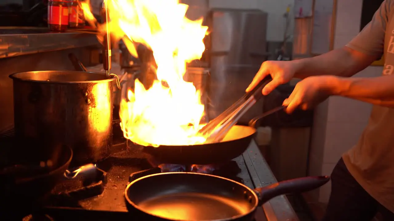 Local Asian street food culture professional chef stir frying fresh ingredients with burning flames and aromatic smokes authentic and traditional hawker centre handheld close up shot