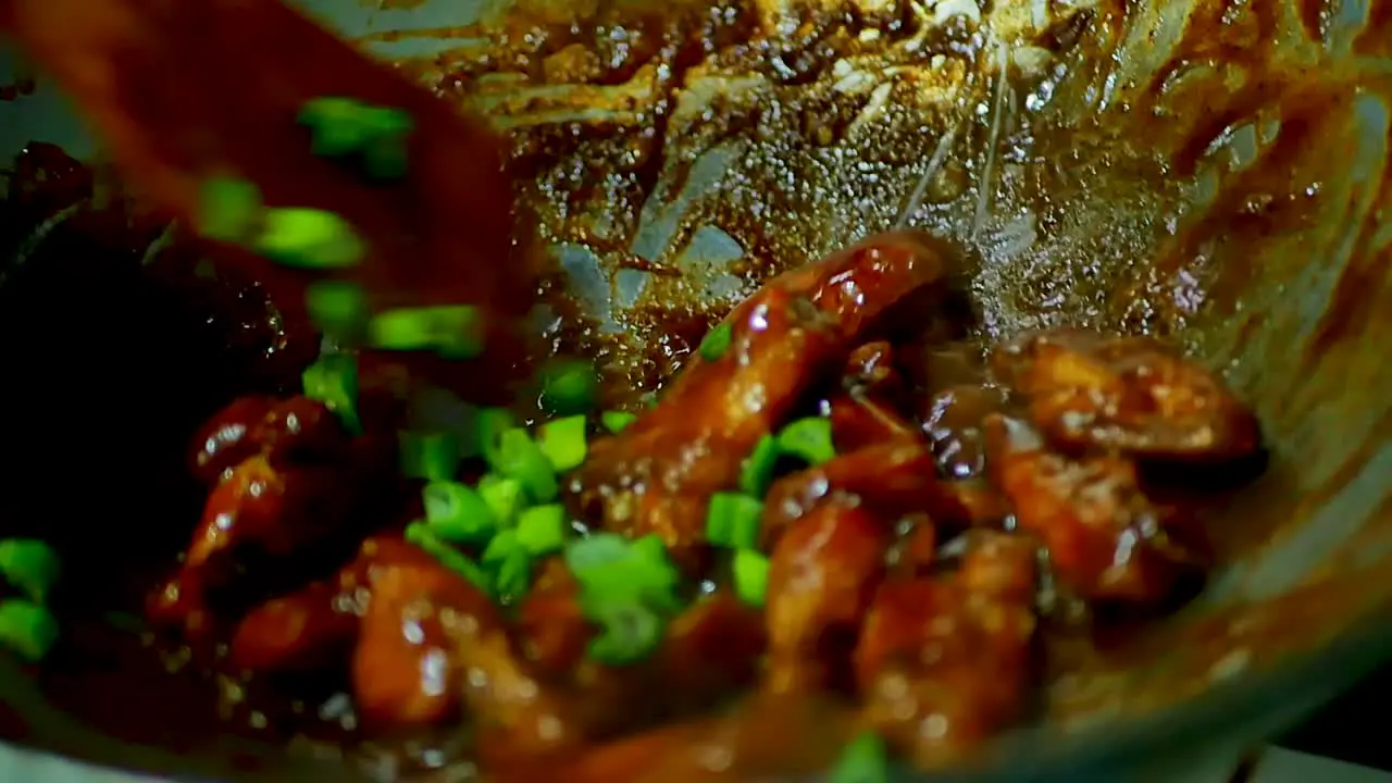 Chicken Wings sizzling in a pan with green onion over a hot stove static shot