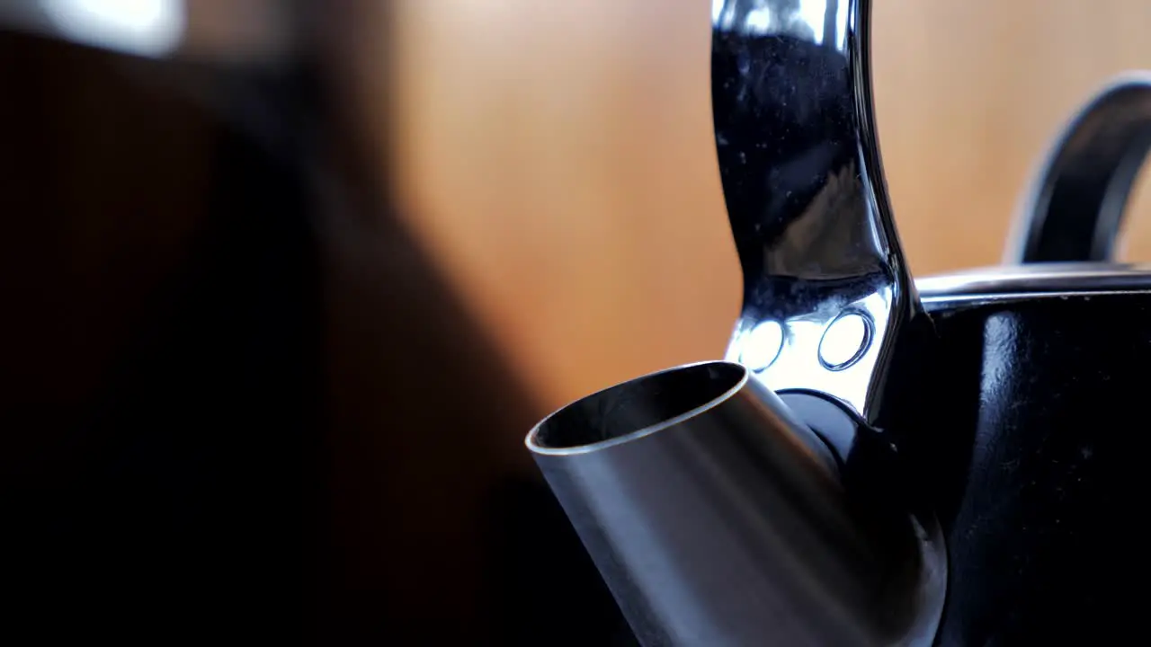 Tight up close shot of black household domestic kitchen kettle slowly boils for cup of tea coffee with steam water vapor coming out of metal spout