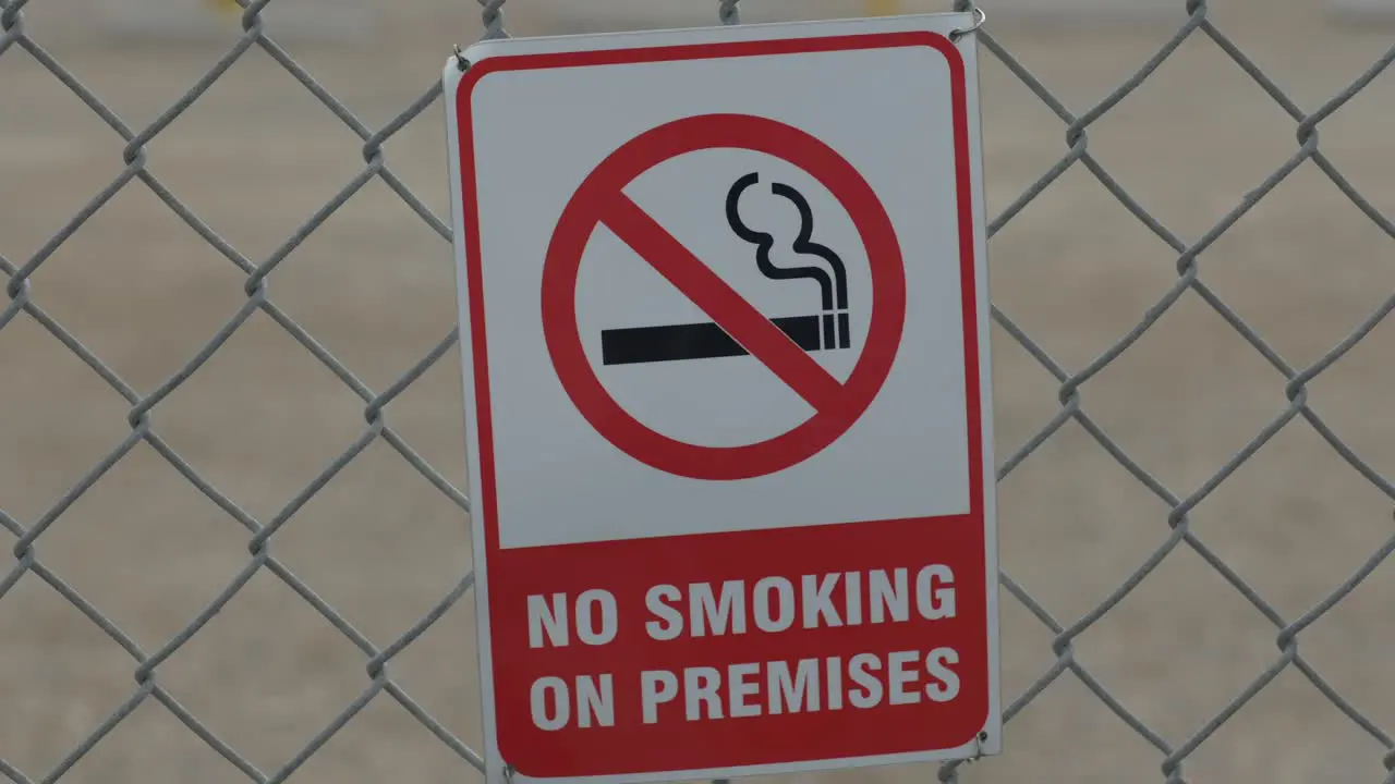 A quick zoom in on a red and white no smoking sign that is behind a chain linked fence