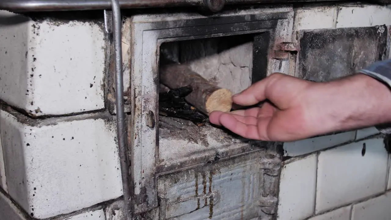 Man opens the door and puts wood in a rustic old kitchen stove