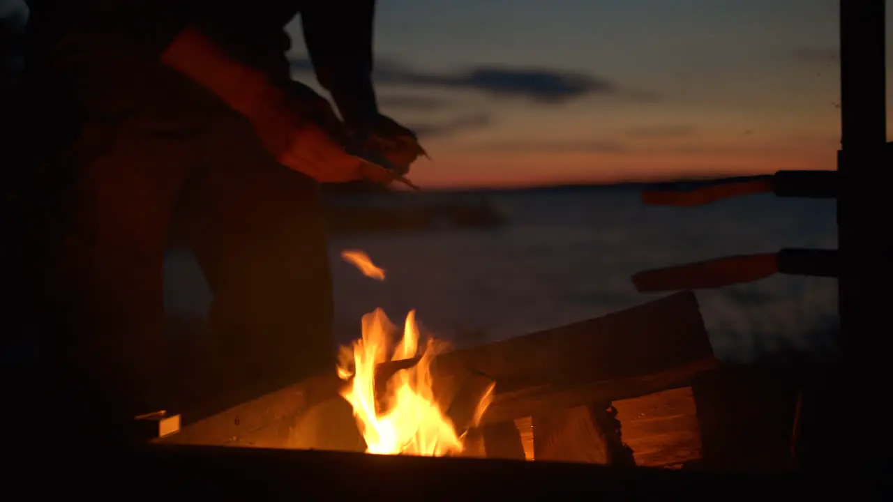 Man lighting camping fire by the sea at dusk