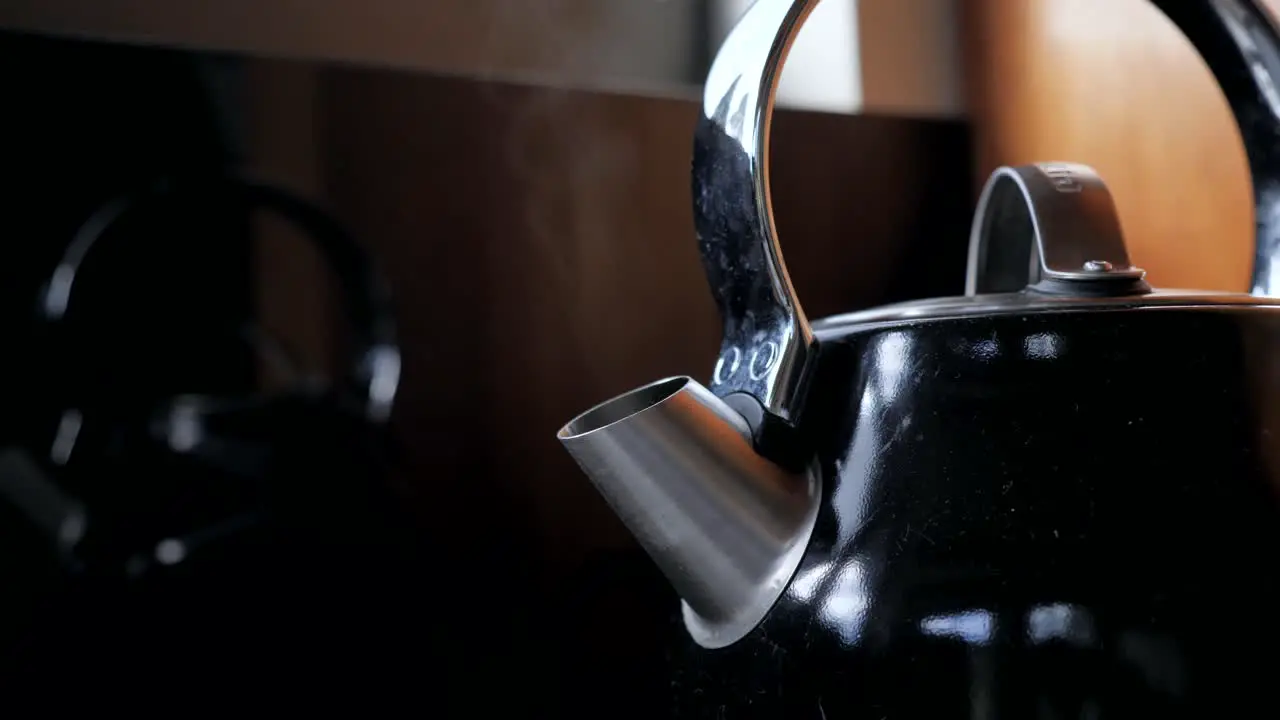 Fixed shot of black household domestic kitchen kettle slowly boils for cup of tea coffee with steam water vapor coming out of metal spout