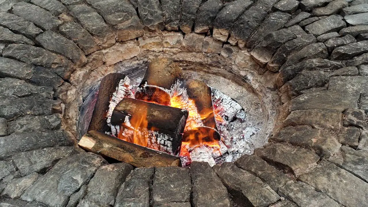 Beautiful circular stone fire pit with flames hot coals and burning logs during a cold Winters day outdoors in the garden