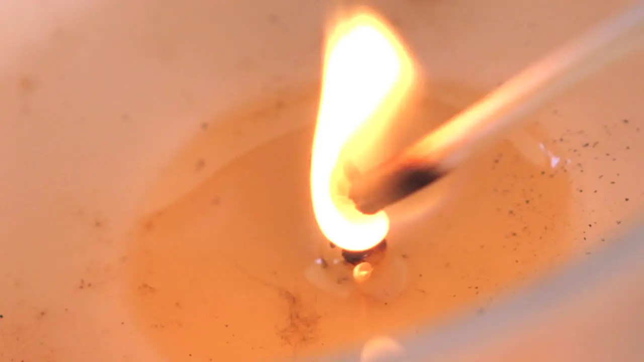 Slow motion macro footage of candle wick being lit by wooden match to burn with bright orange flame flickering in soy wax