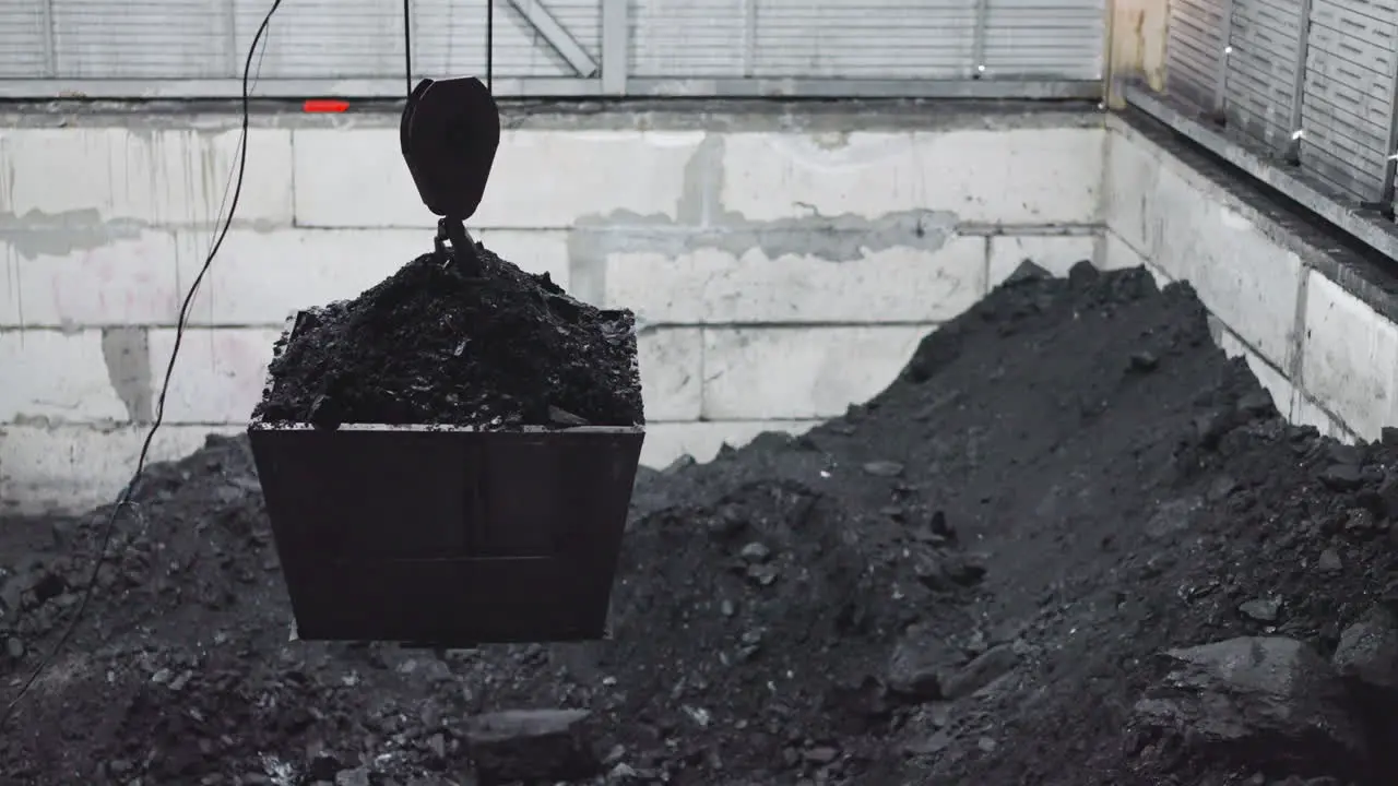 Bucket with charcoal hangs on crane hoist over storage pool