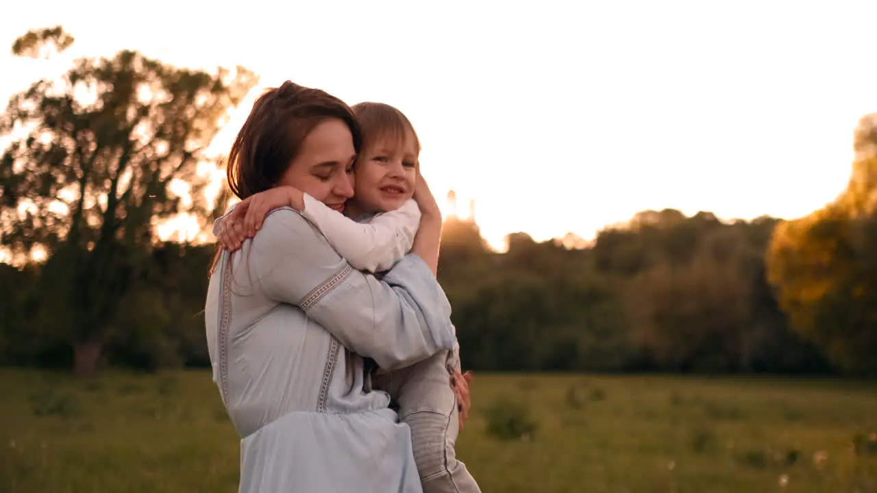 The son kisses his mother sitting at sunset in a field hugging and loving mother Mother's day