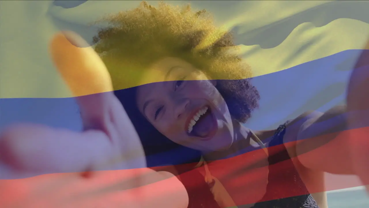 Animation of colombian flag waving over biracial woman talking selfie video through camera at beach