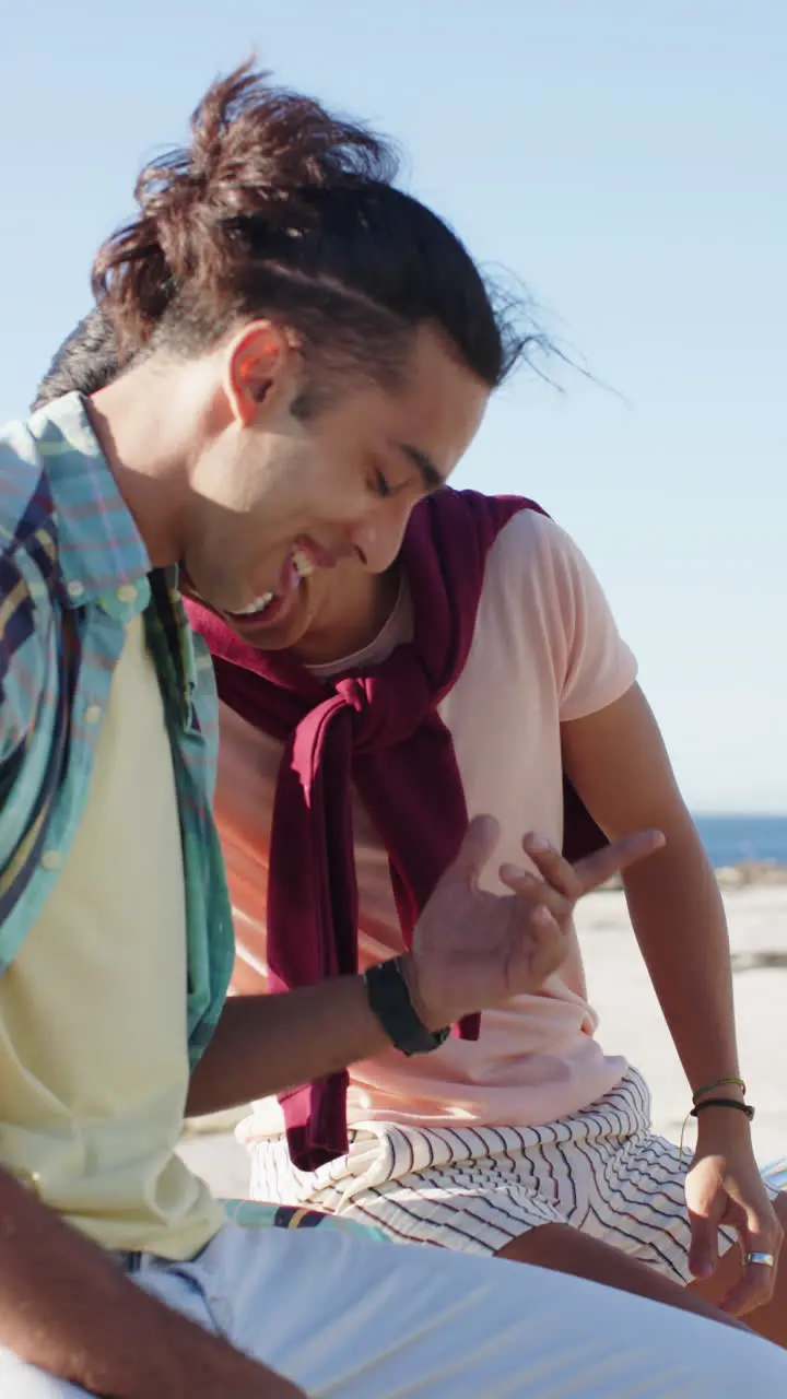 Vertical video of happy diverse male couple embracing at promenade by the sea slow motion