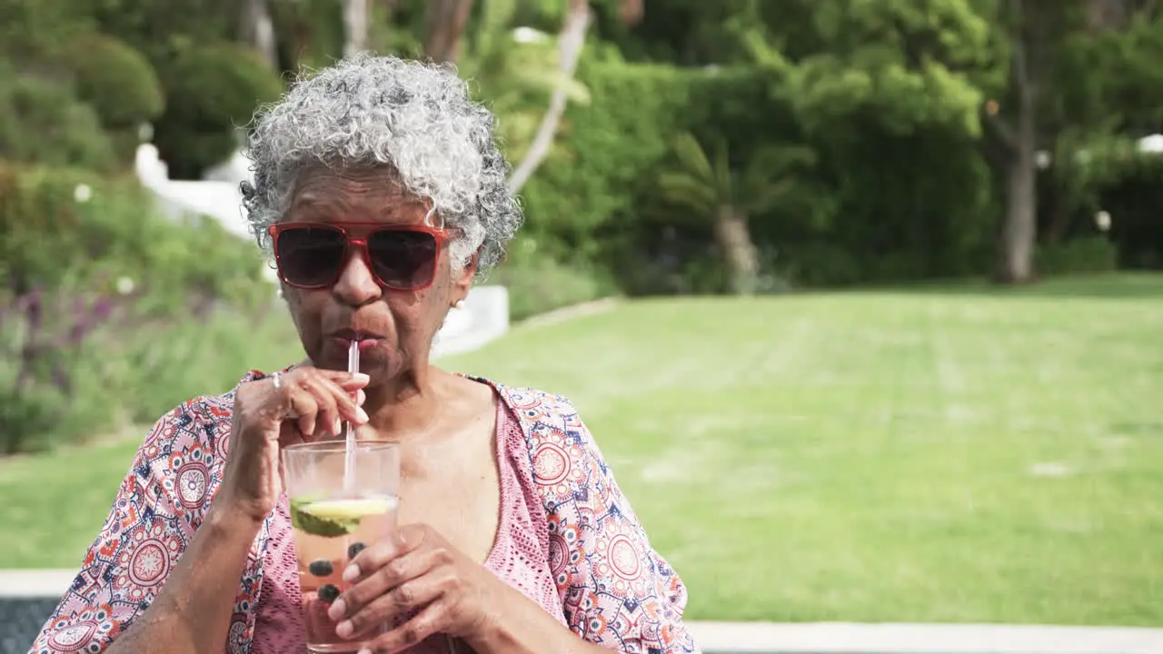 Senior african american woman in sunglasses drinking cocktail in garden copy space slow motion