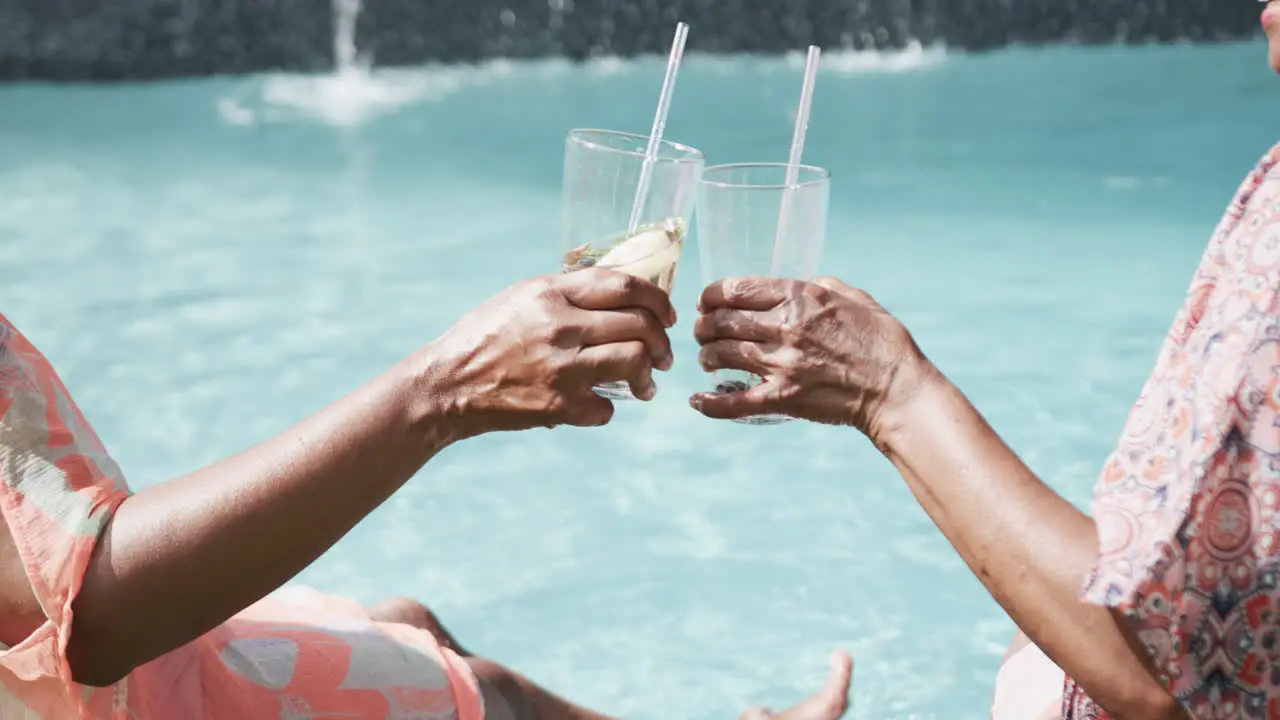 Midsection of senior african american female friends sitting by pool making a toast slow motion