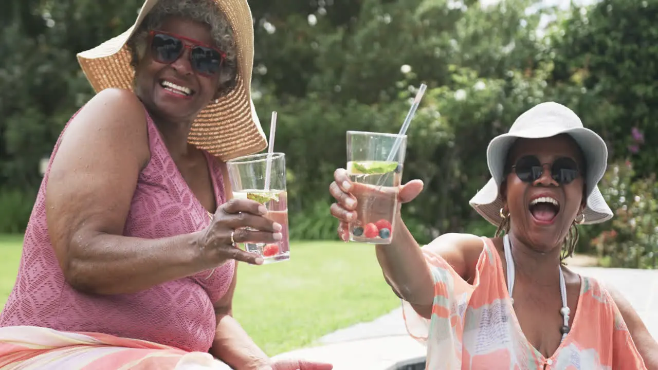 Portrait of senior african american female friends in sunhats making a toast in garden slow motion