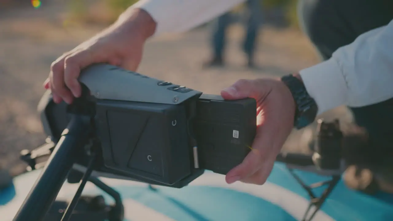 A person putting batteries on a drone with plants and dirt in the background