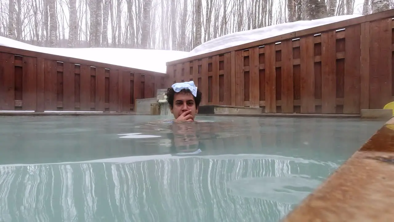 Foreign male tourist inside open air onsen in winter landscape in Japan