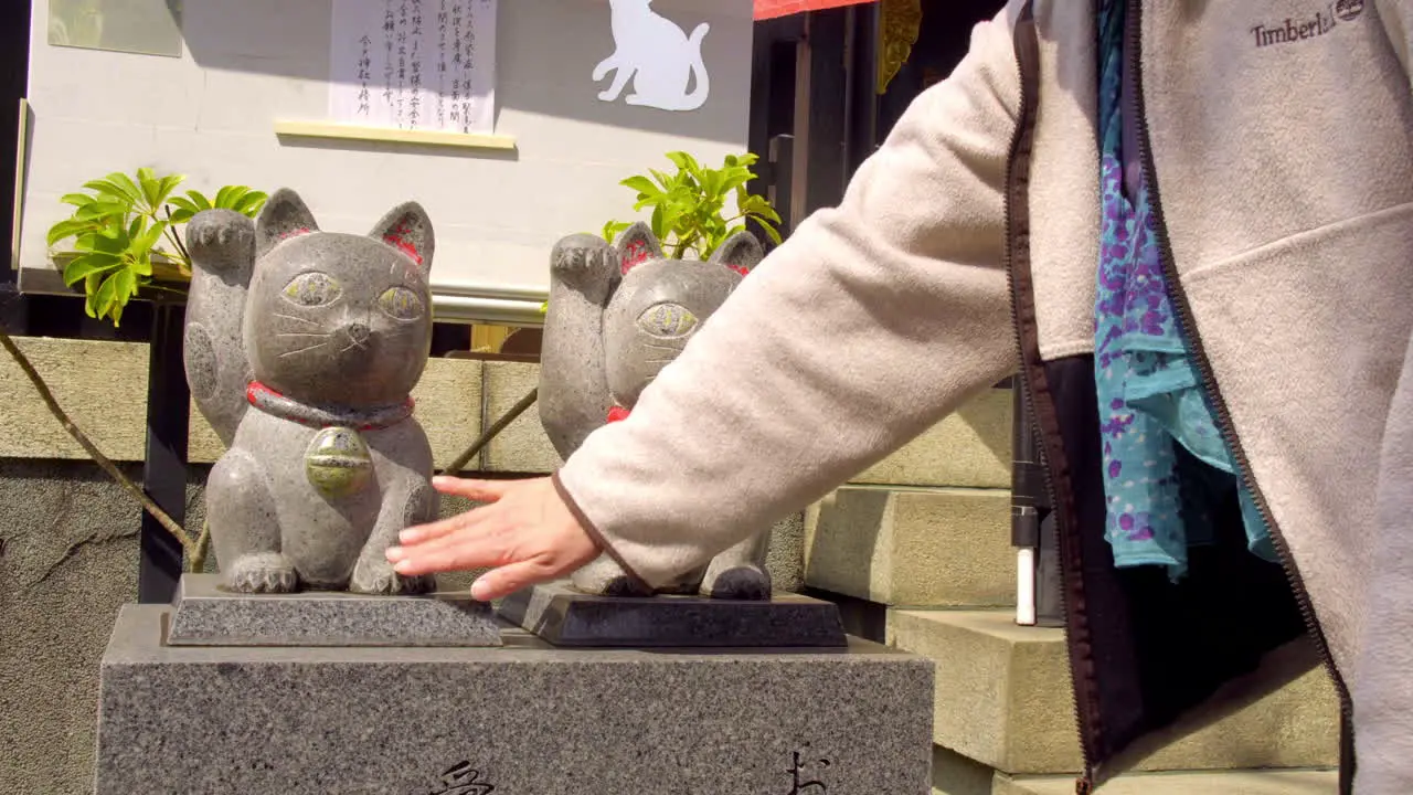 TOKYO JAPAN circa April 2020 man worshipping at traditional Japanese shrine patting pair of lucky cats for good fortune in sunny spring day