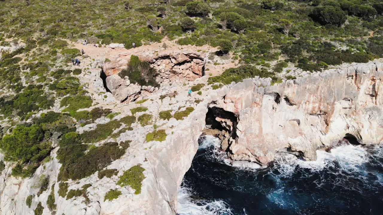 Drone shot flying to the right capturing a sea arch with tourists walking around near Cala Varques in Majorca