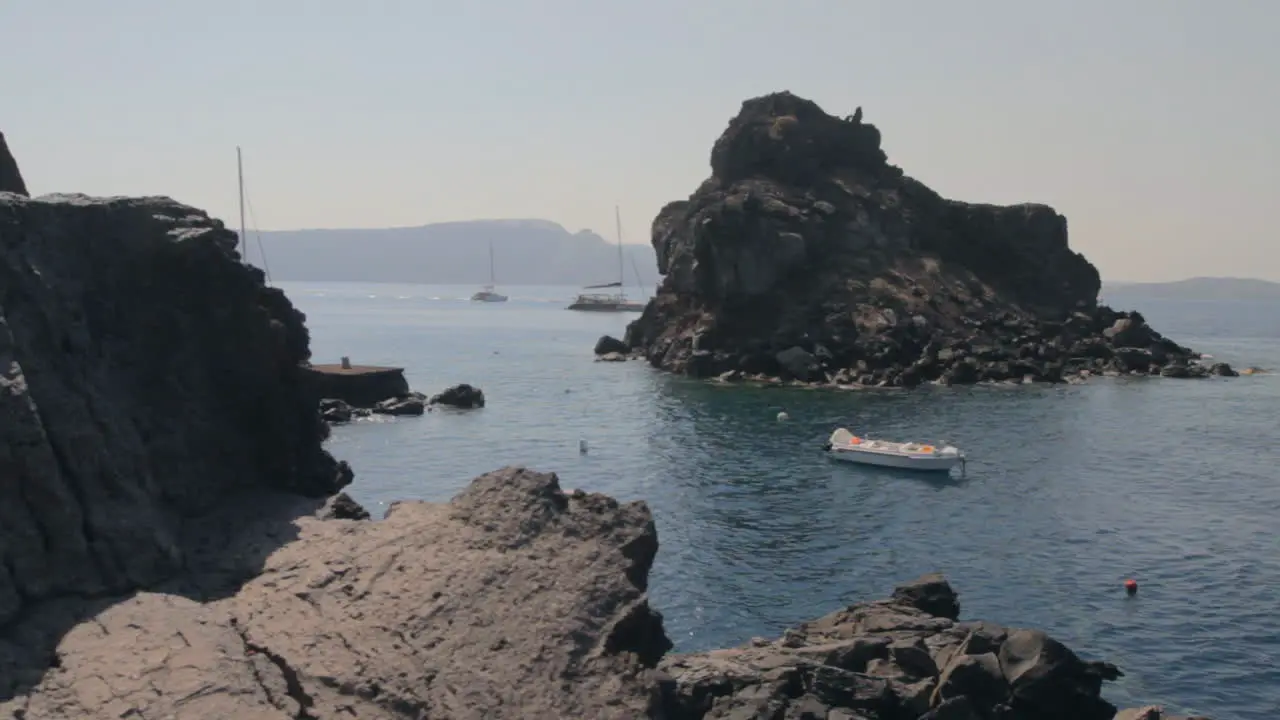 A rocky beach within the Santorini caldera with catamarans floating around it