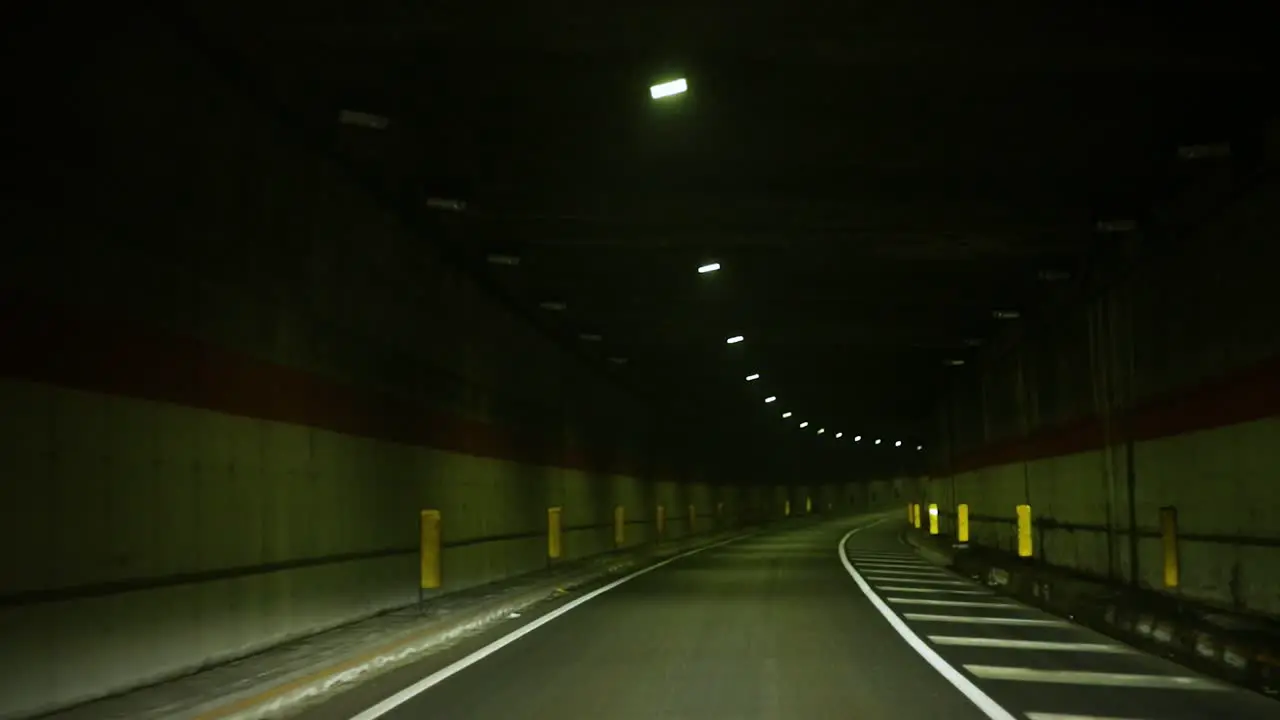 POV of a car driving slowly through a dark and long tunnel at night