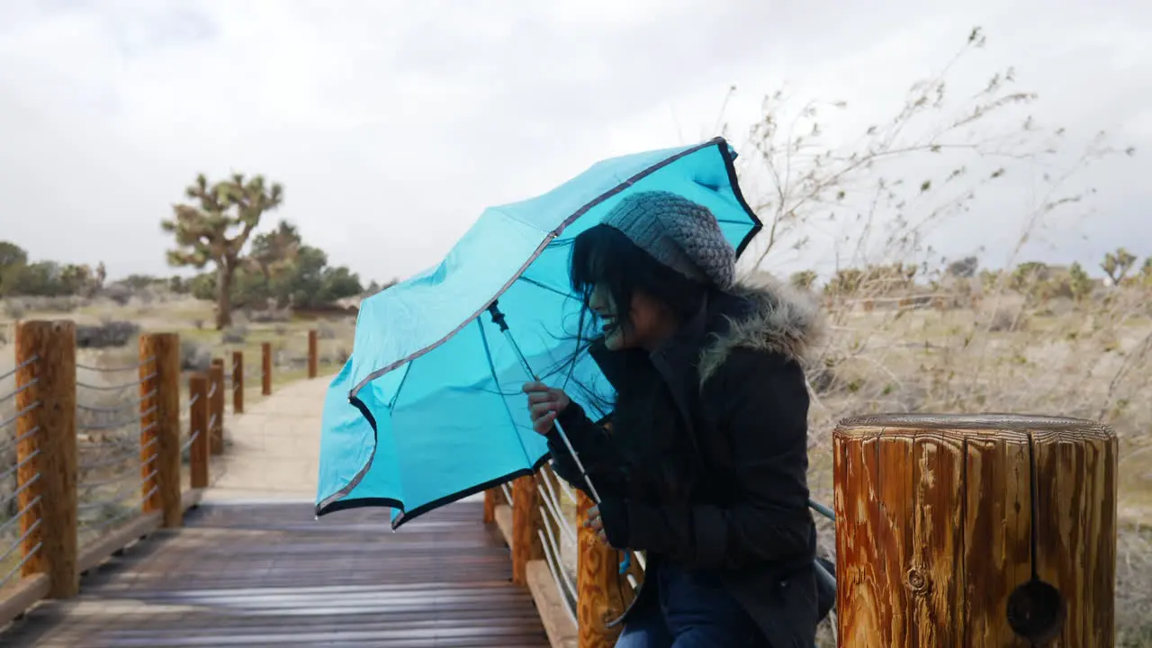 A pretty young woman smiling in bad weather with a blue umbrella during a rain storm with strong wind