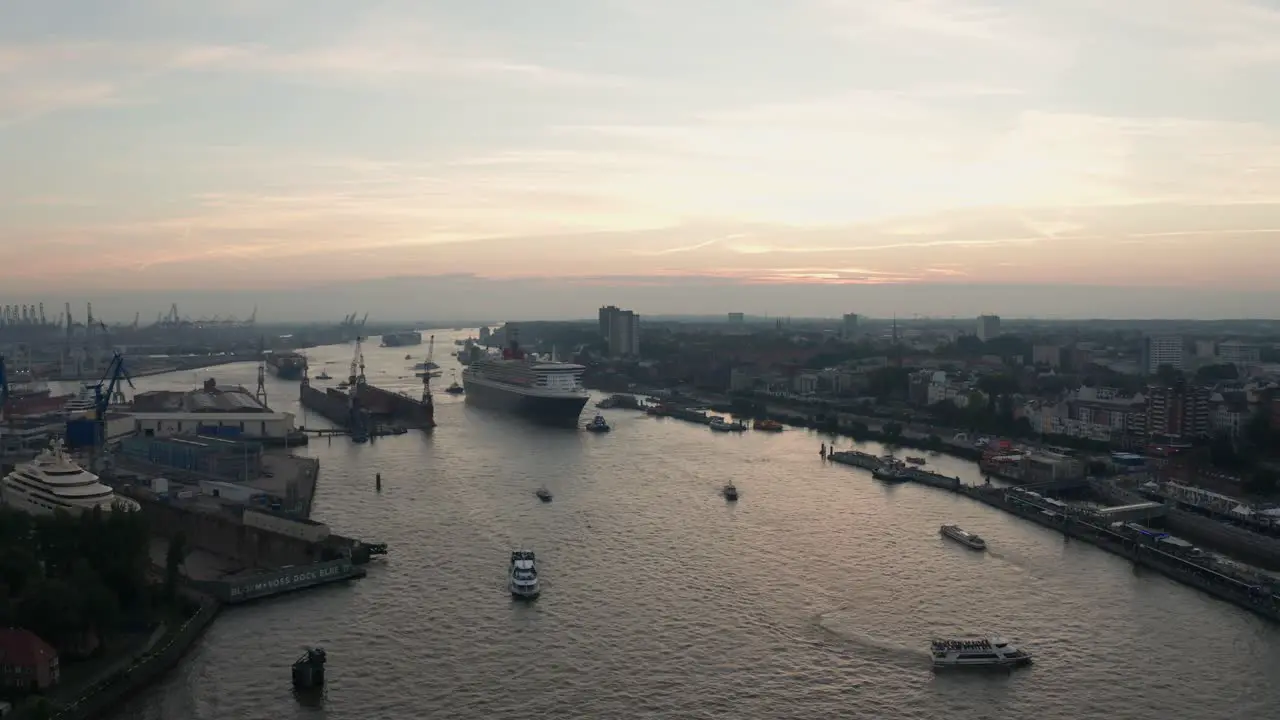 Drone Shot Hamburg Harbour Queen Mary 2 entering the harbour during sunset golden hour at cruise days with skyline in the background