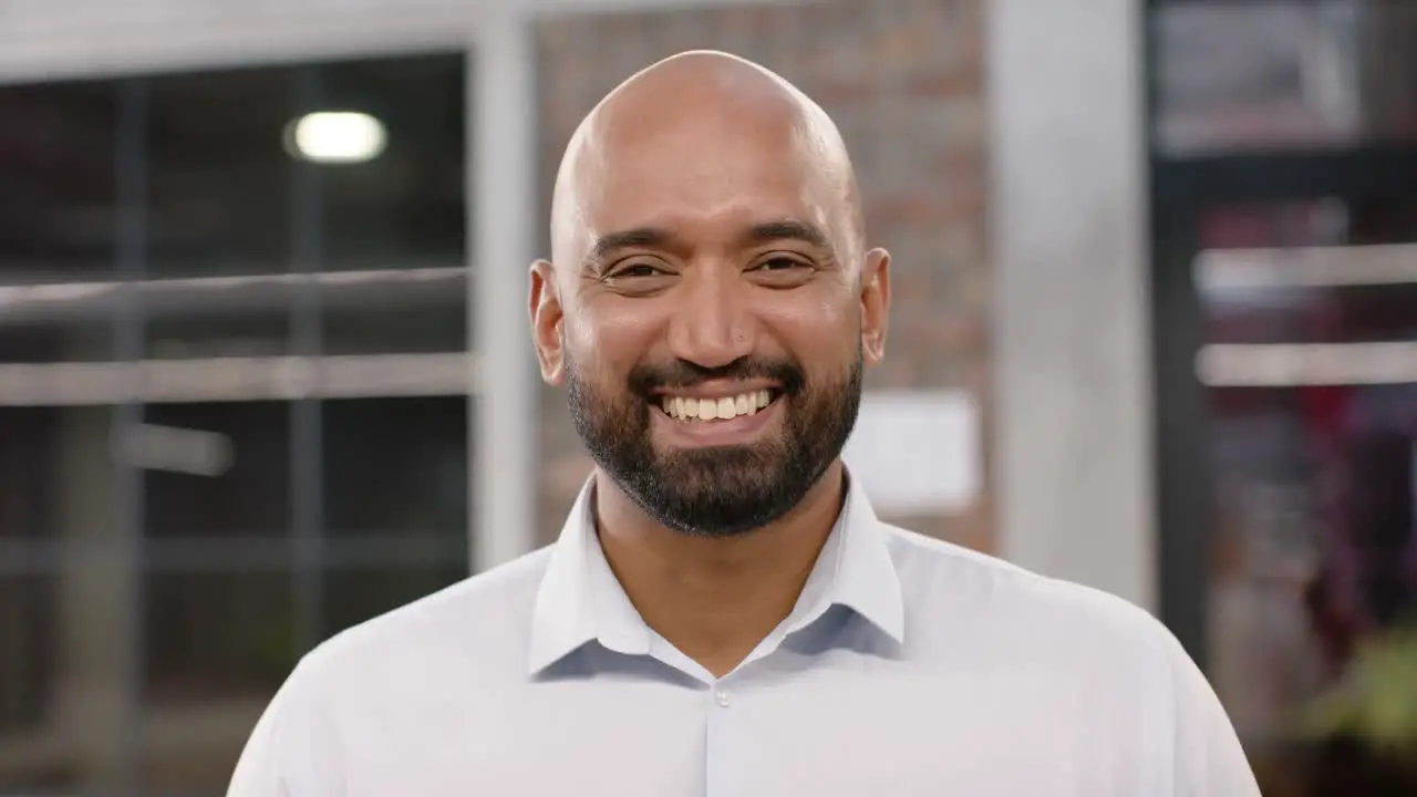 Portrait of happy biracial bald creative businessman with beard smiling in office in slow motion