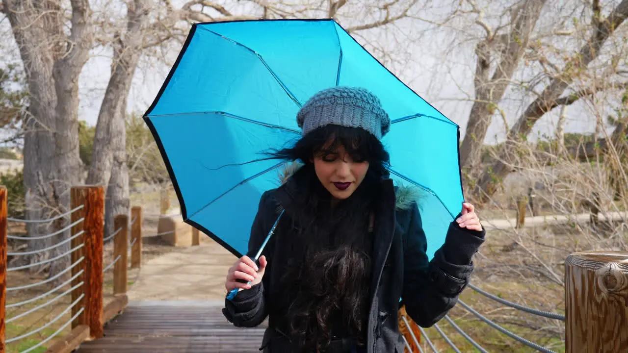 A pretty woman looking cute and smiling with a blue umbrella during a break in the rain storm in slow motion