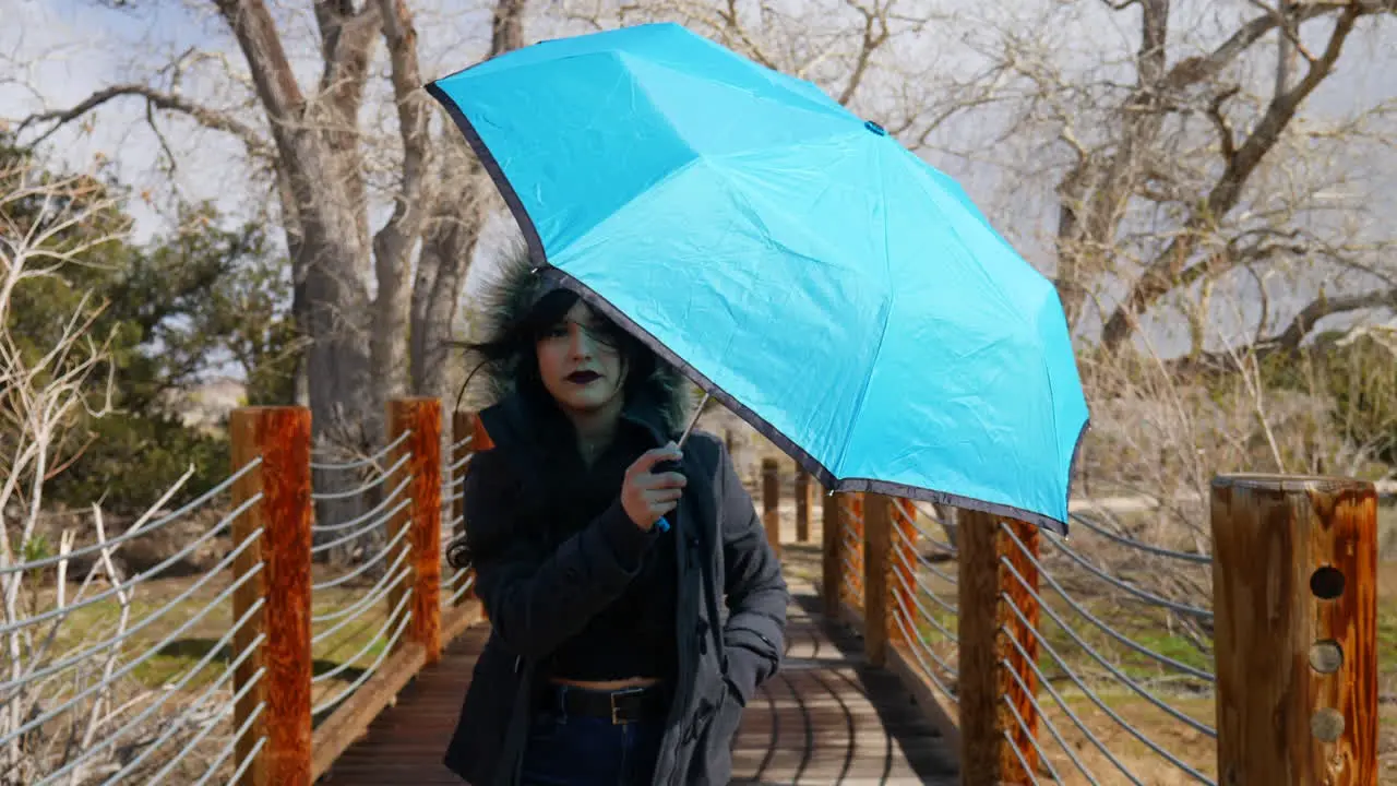 A pretty woman walking with a blue umbrella across a bridge during bad weather and a rain storm SLOW MOTION