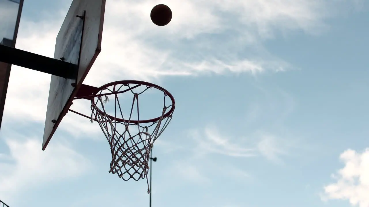 Man dunking a basketball outside against a blue sky