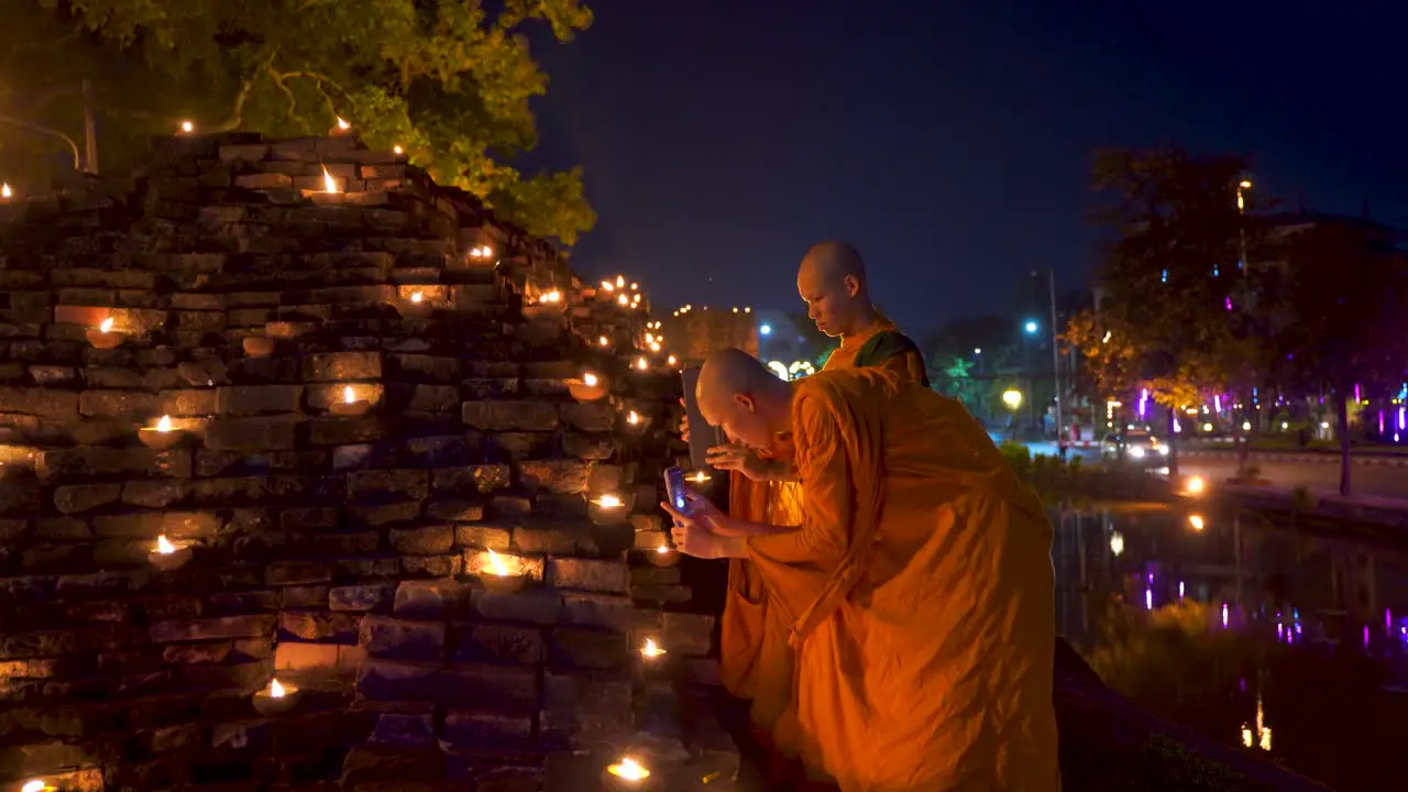 Two young Thai monks in Orange robes taking pictures of candles during Yi Peng Festival