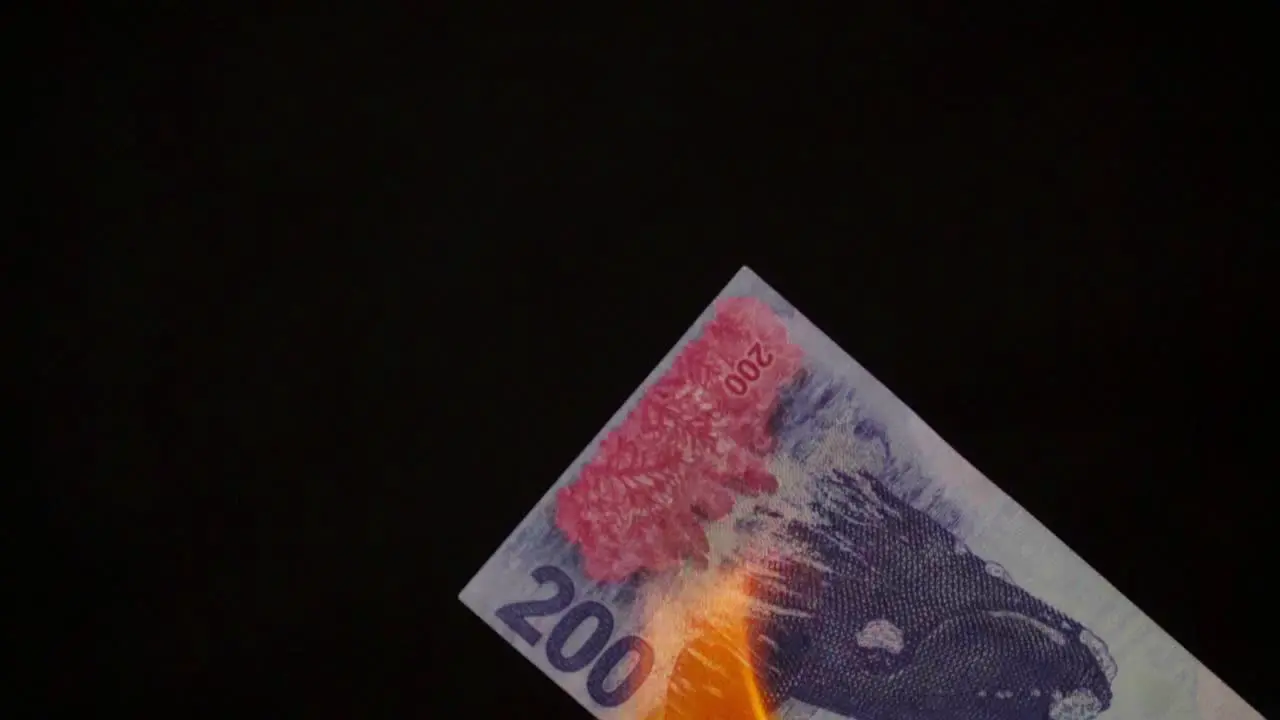 Close-up of a burning Argentinian 200 pesos bill illustrating the rising cost of living