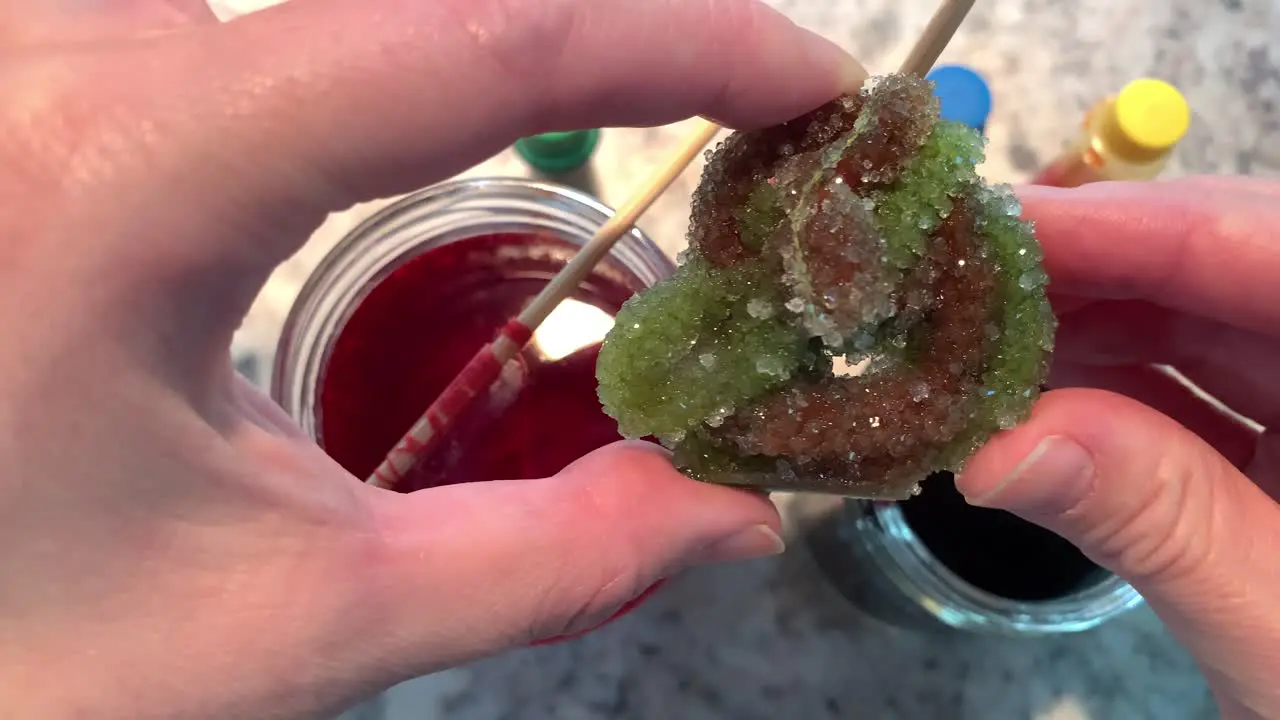 A hand holding a sparkly Borax crystal with green and purple colors