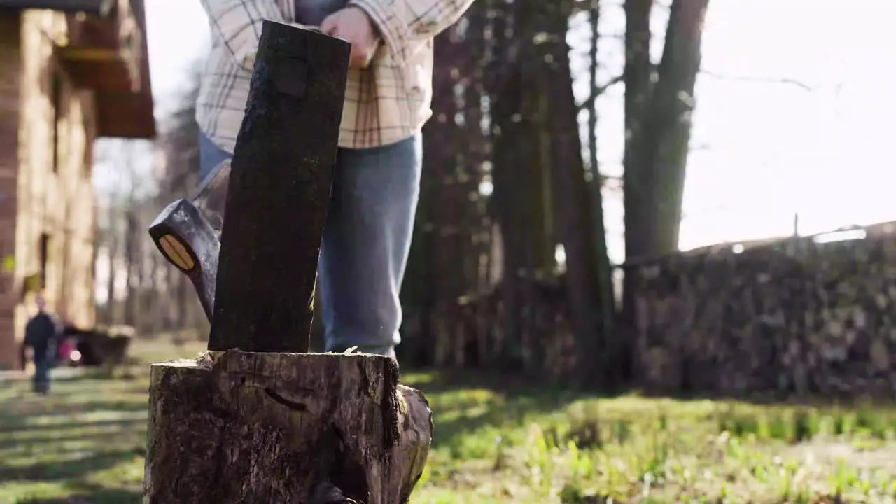 Bottom view of caucasian man chopping firewood with an ax outside a country house Then he looks at camera