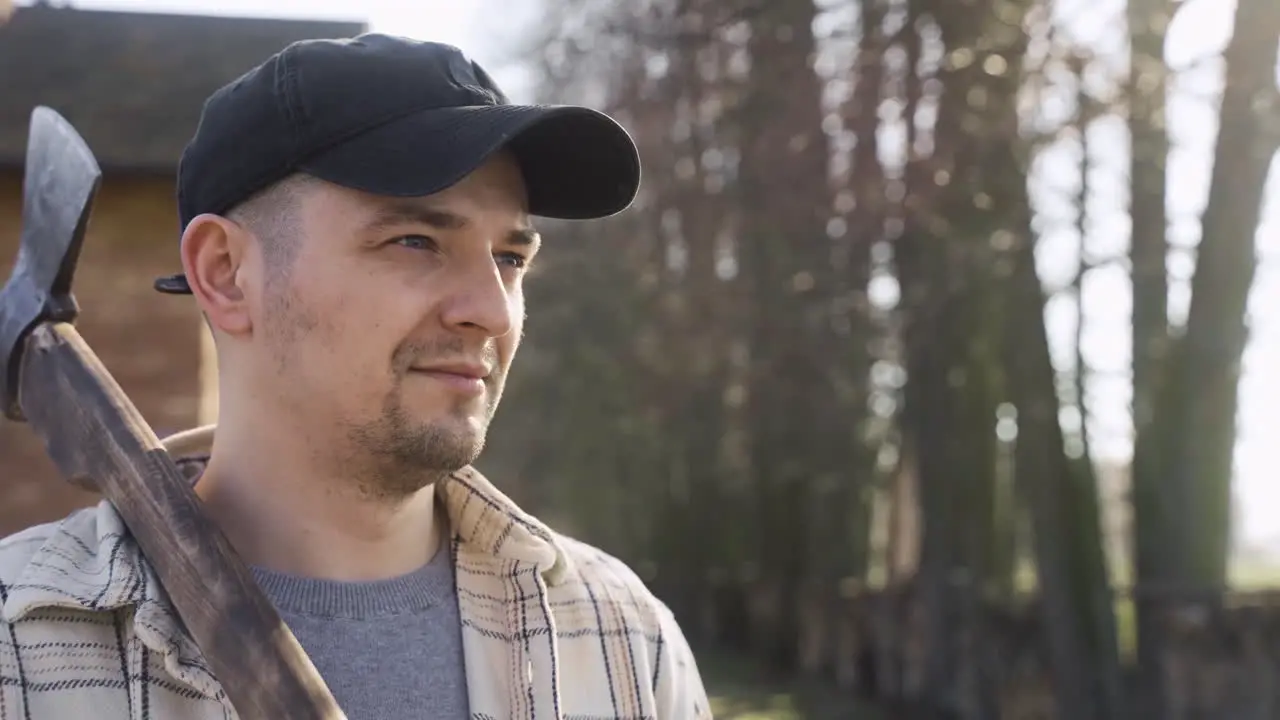 Close-up view of caucasian man holding an ax outside a country house while smiling and looking at camera