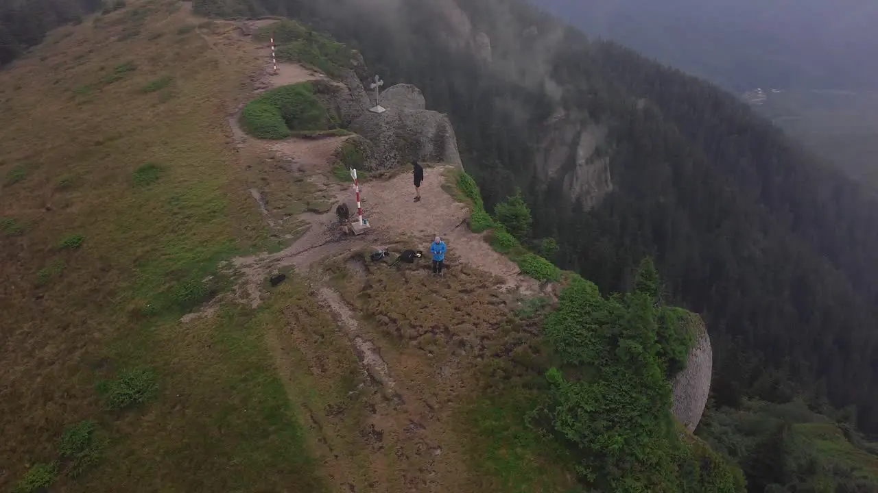 Aerial helix drone shot of three hikers on a mountain summit near a steep cliff