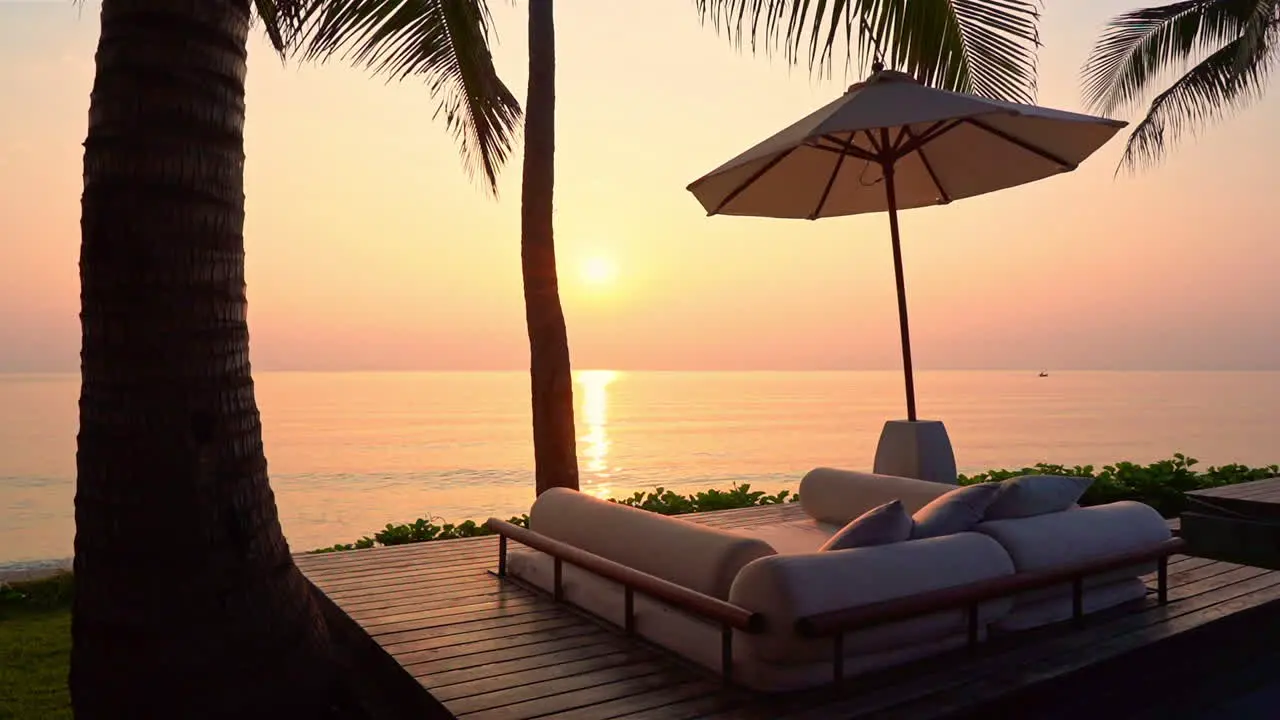 Seaside lounge with bed and beach umbrella silhouette on the picturesque orange sunset over the sea