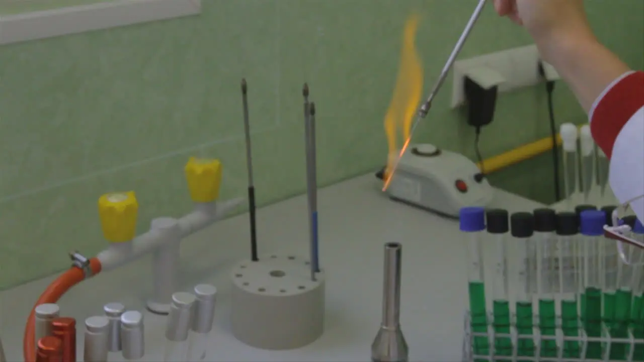 In a science laboratory a colorful orange flame is created when a chemical reaction occurs around a thin pipette that the scientist holds above an open flame