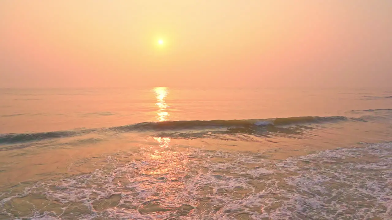 Slow motion shot of orange and peach sunrise over ocean with breaking waves