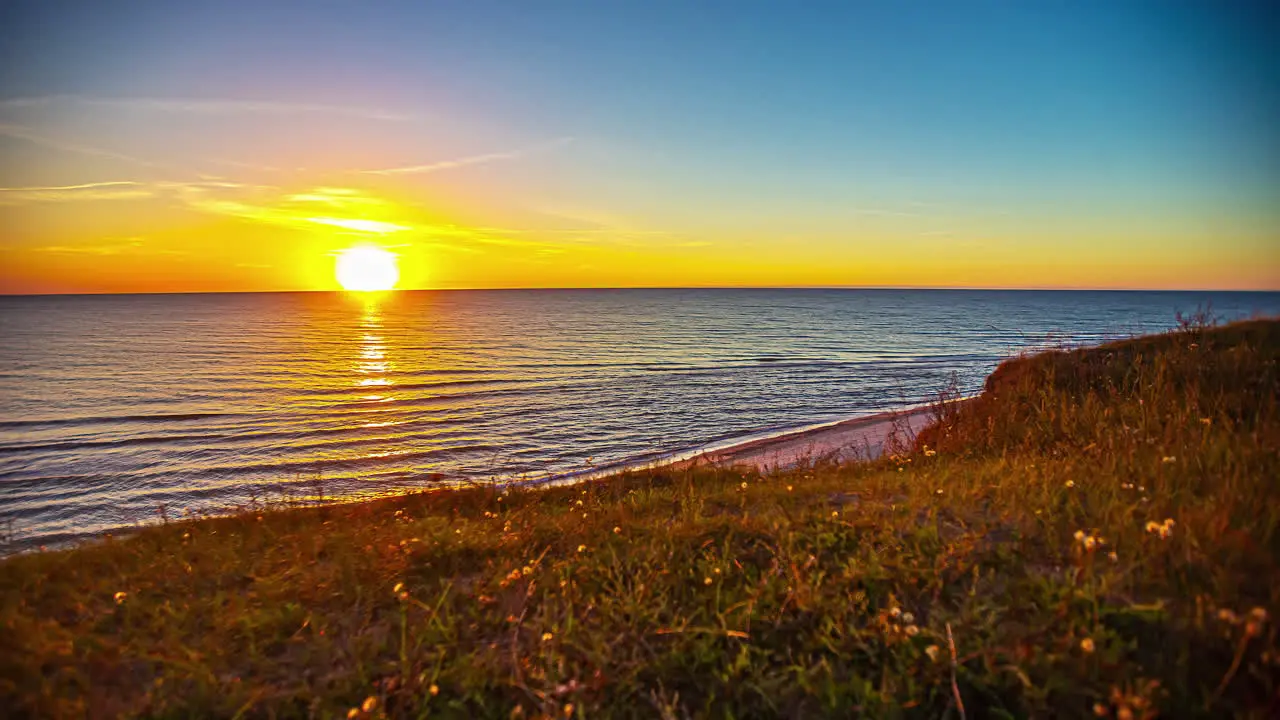 Golden sunset on the horizon of the ocean with gentle waves on the beach time lapse