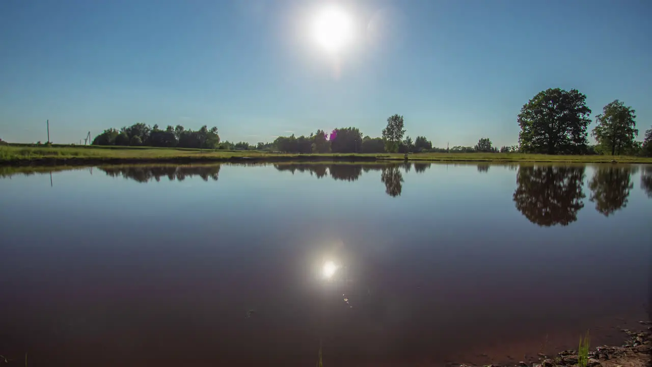 Cool timelapse of the sun setting and then rising behind the trees on a summer day and a still lake reflecting everything