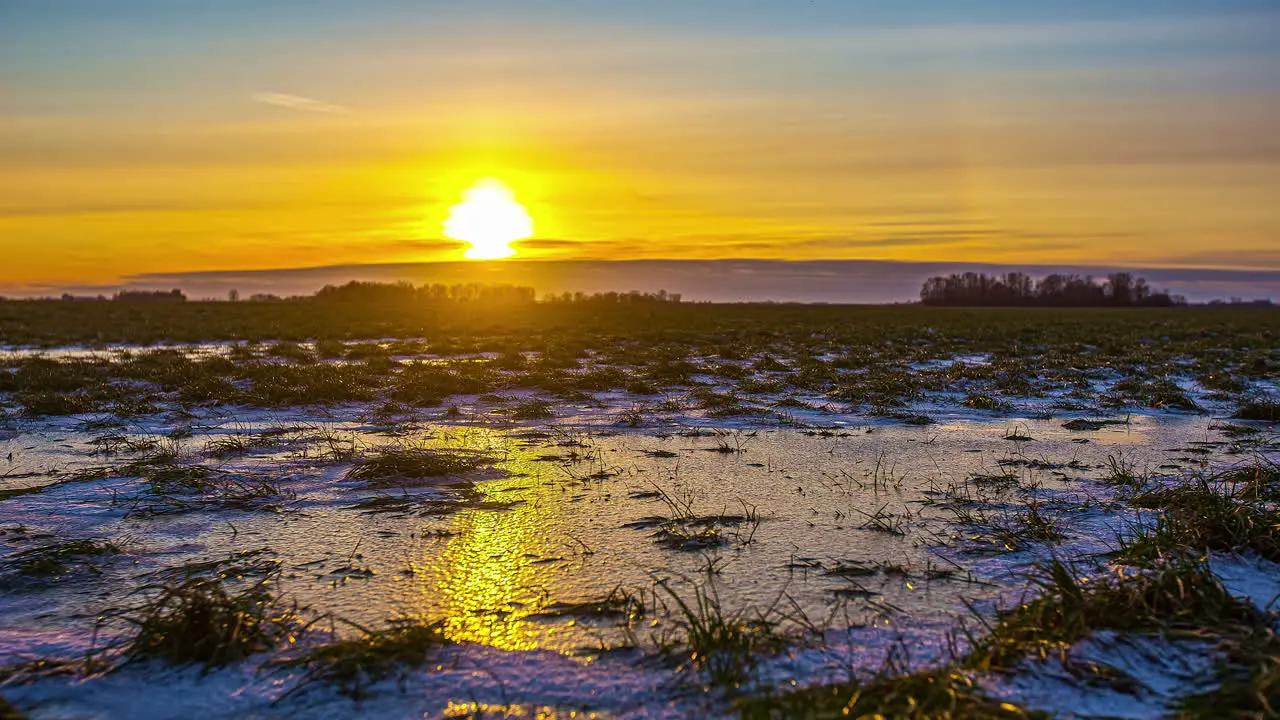 Time lapse shot of snowy and frosty farmland with epic golden sunset at horizon