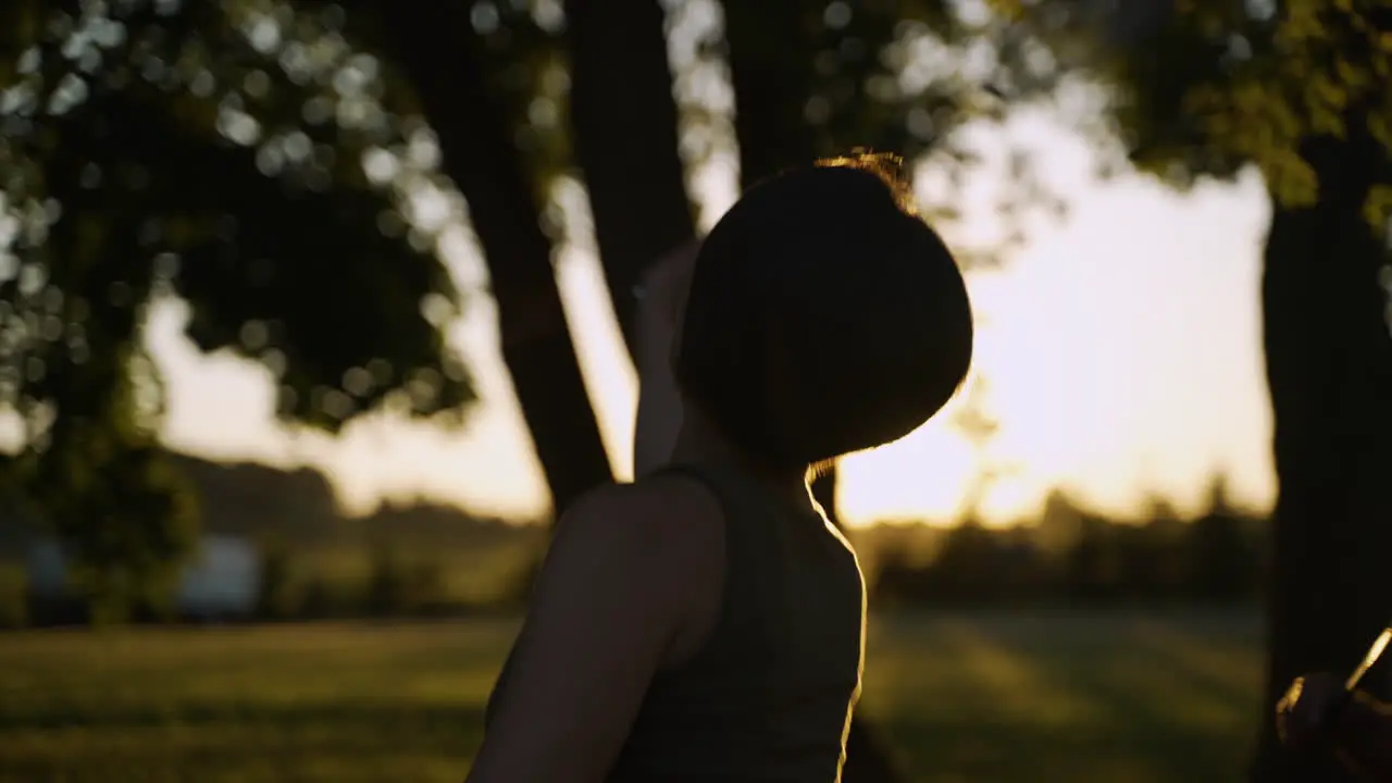 Woman with short hair in a tank top plays badminton in a field as the sun sets in the background