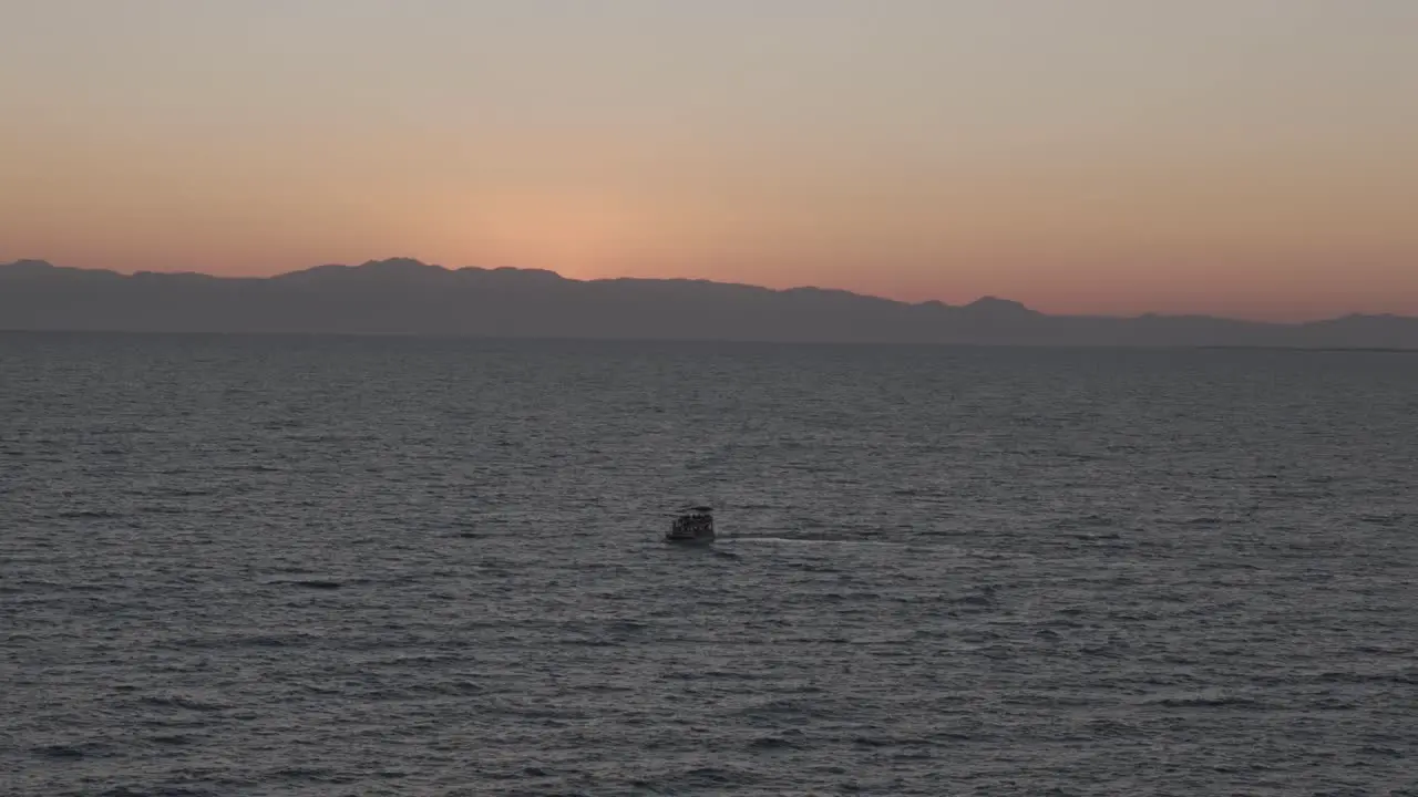 Small sailing boat travelling across Mediterranean sea towards glowing orange sunset skyline